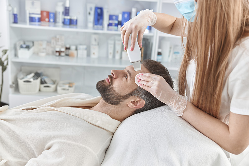 faciales_0002_bearded-man-smiling-in-professional-beauty-spa-salon-during-ultrasonic-facial-cleansing-procedure